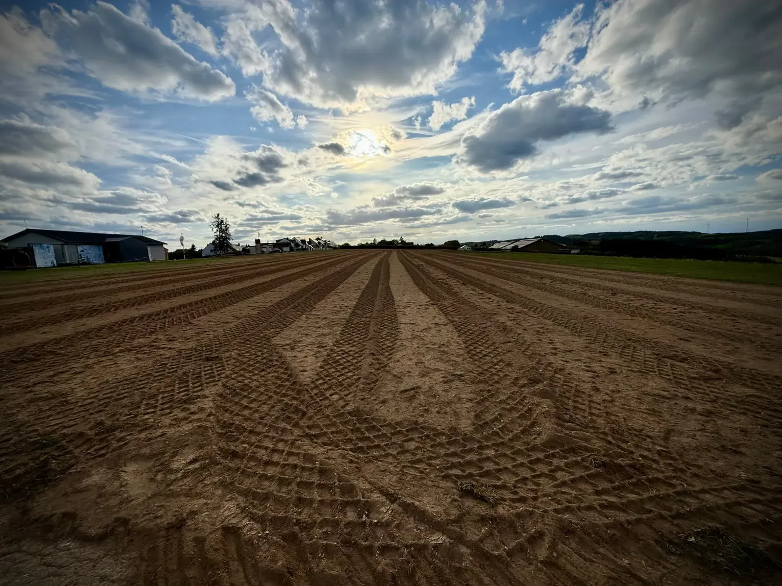 Walzenspuren über die gesamte Breite der gepflügten Piste, am Horizont die Hallen und das Dorf