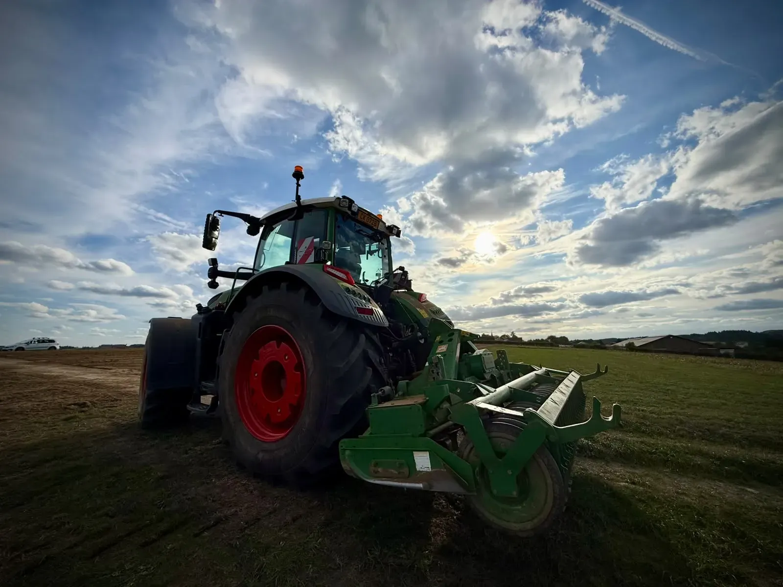 Ein Traktor mit Anbaugerät am Feldrand in der tief stehenden Abendsonne