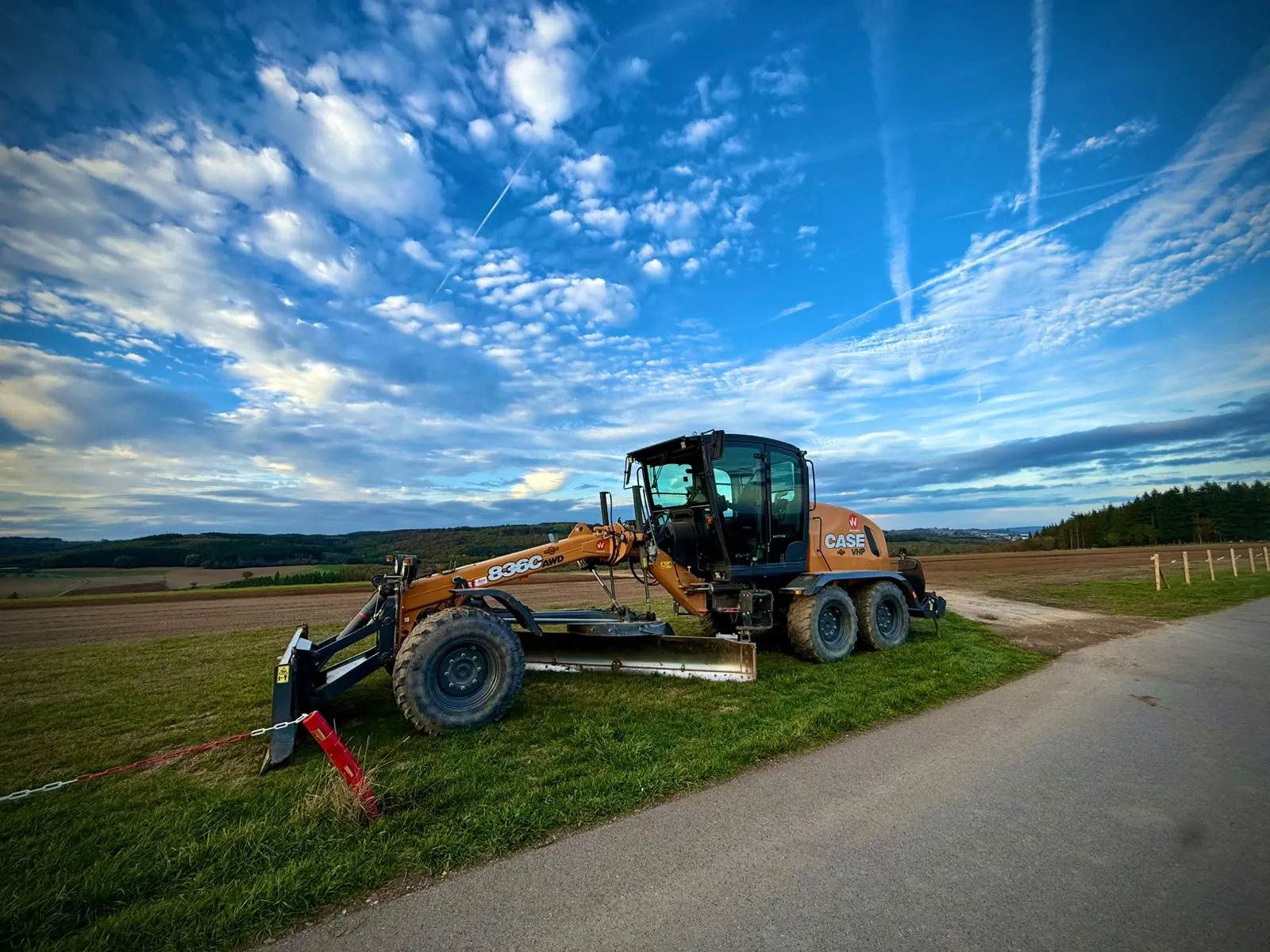 Une niveleuse jaune garée sur l'herbe à côté de la piste, sous un ciel bleu avec des nuages
