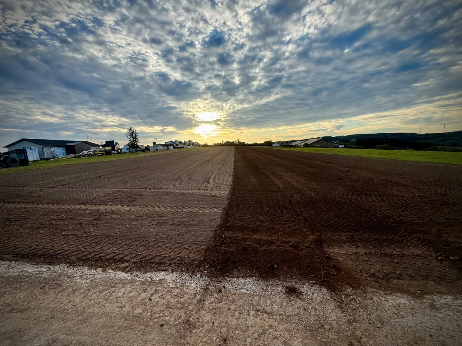 La piste en terre préparée, vue dans l'axe vers les hangars et le village au coucher du soleil